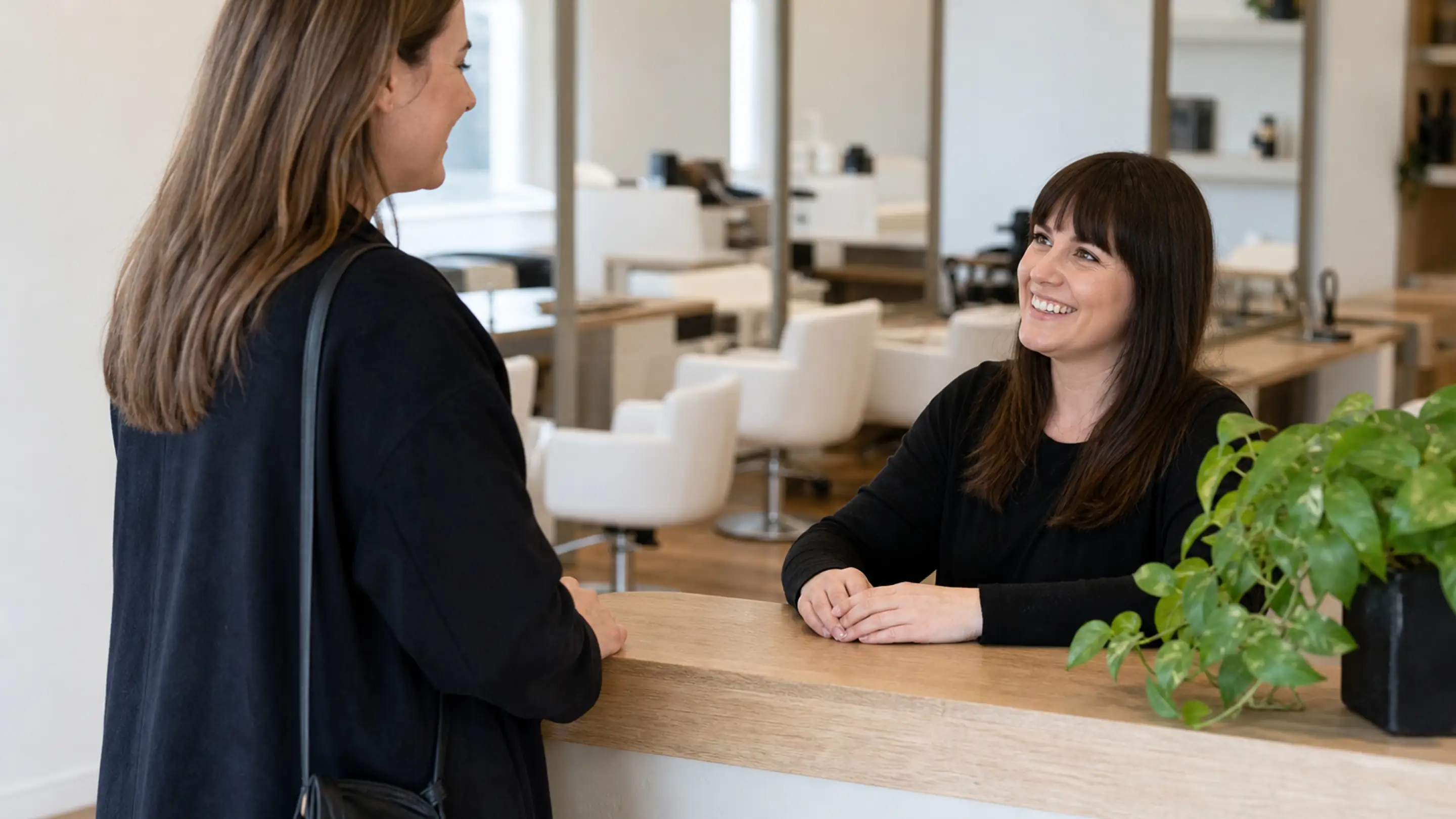 A client being warmly welcomed at a salon front desk, the kind of relaxed moment where permission is asked properly.